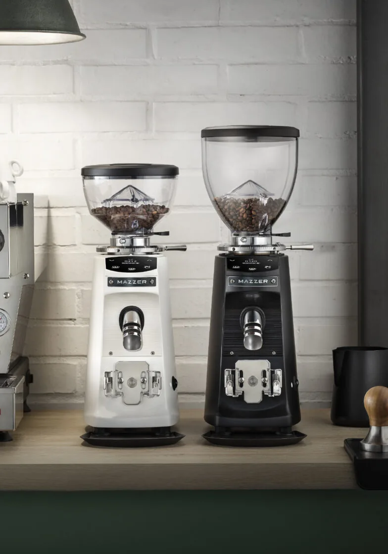 To Mazzer Mini Electronic, en hvit og en svart, side om side på en benk ved en murvegg