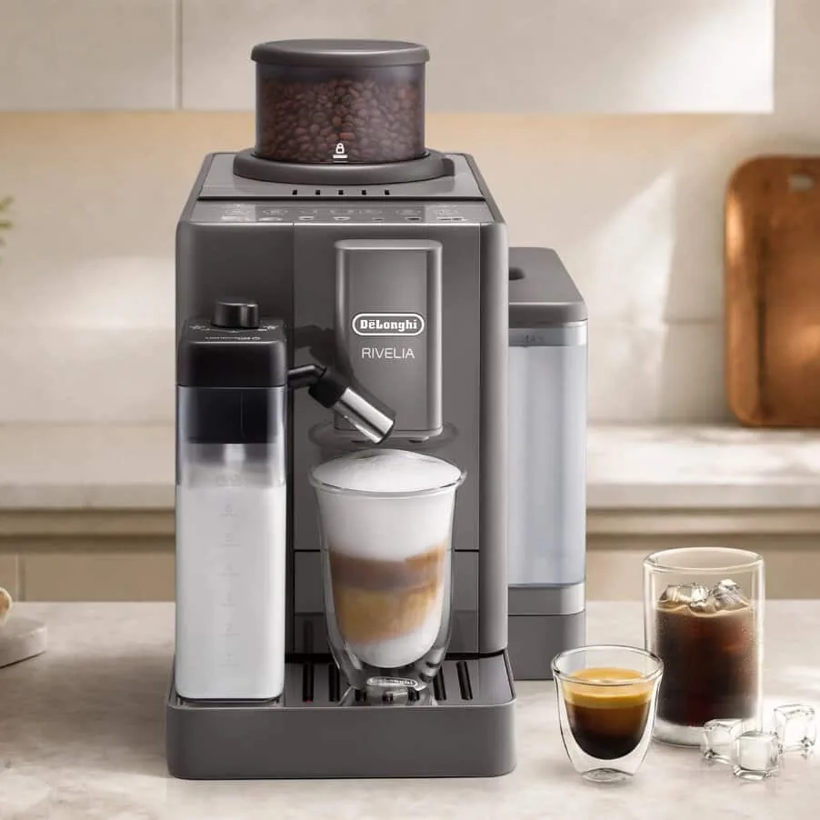 De'Longhi Rivelia i mørk grå på en kjøkkenbenk, med melkekanne, en cappuccino og iskaffe i glass
