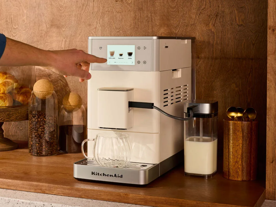 En hånd peker på berøringsskjermen til en porselenshvit KitchenAid KF4 på en kjøkkenbenk av tre