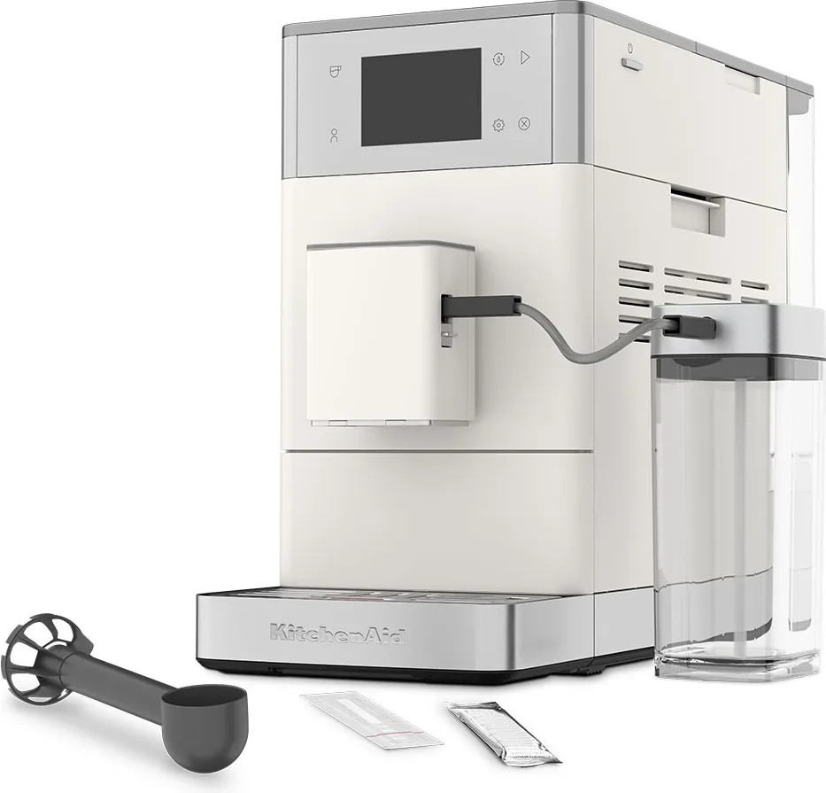 KitchenAid KF4 i porselenshvit sett skrått forfra, med melkebeholder, kaffeskje og teststrimmel foran