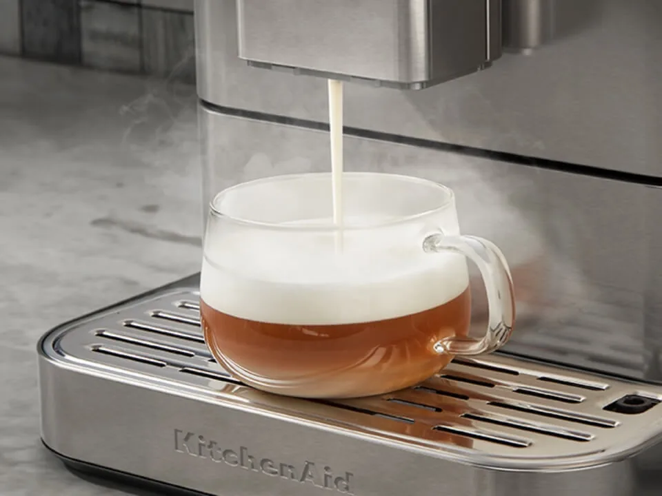 Varm melk renner fra utløpet på en KitchenAid KF6 i rustfritt stål ned i et glass