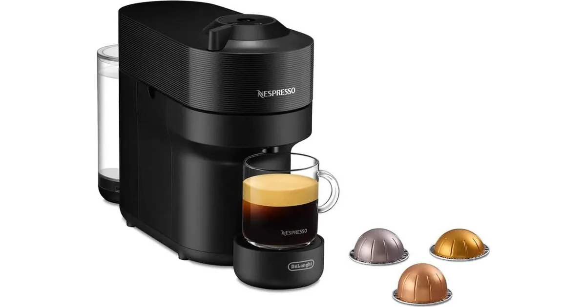 Nespresso Vertuo Pop i svart fra De'Longhi, sett skrått forfra, med et glass kaffe og tre Vertuo-kapsler