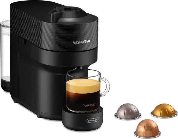 Nespresso Vertuo Pop i svart fra De'Longhi, sett skrått forfra, med et glass kaffe og Vertuo-kapsler