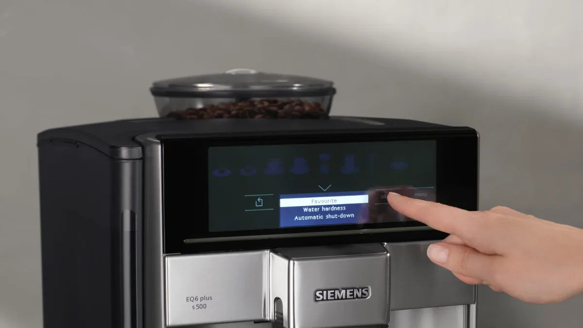 En finger blar i menyen på Siemens EQ6 plus s500, med Favourite, Water hardness og Automatic shut-down