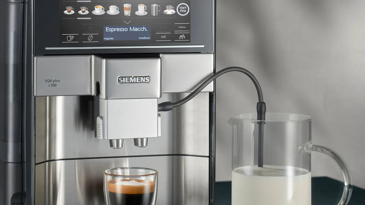 Melkerøret fra Siemens EQ6 plus s700 står i en glasskanne med melk mens en espresso macchiato lages
