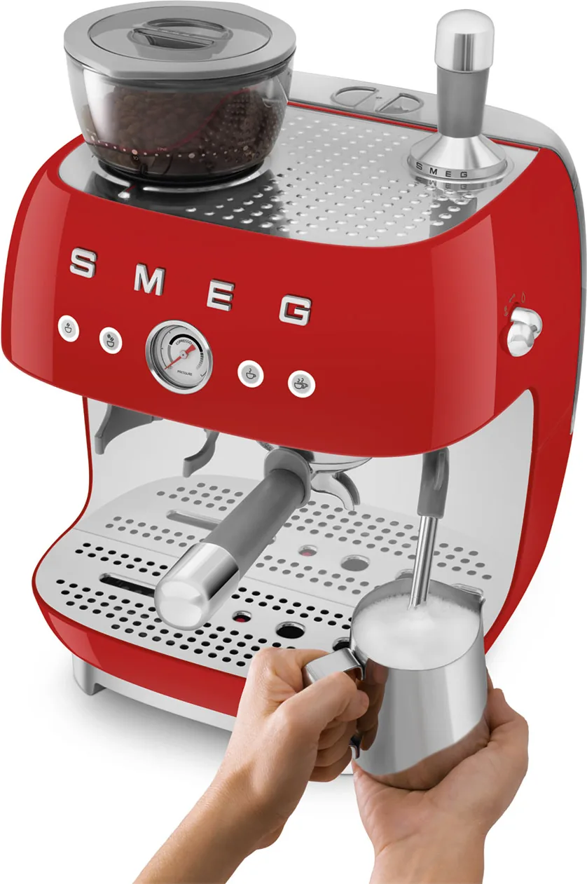 Smeg EGF03 i rødt sett skrått ovenfra, med to hender som skummer melk i stålkannen under damplansen